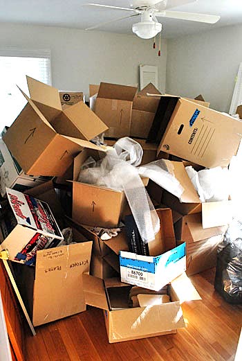 A living room piled with mismatched, half-collapsed cardboard moving boxes