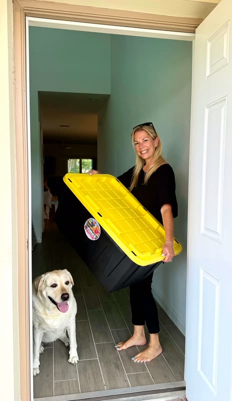 Tina carrying one of her moving totes at a front door, with her yellow lab